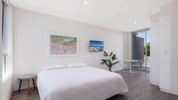 Een moderne slaapkamer met een groot bed, een klein nachtkastje, een kamerplant en uitzicht op de omgeving door een schuifdeur.