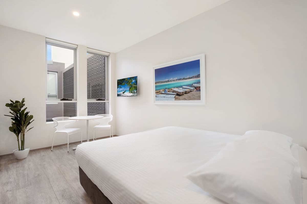 Un dormitorio moderno con una cama grande, una mesita, dos sillas, una planta en maceta y dos cuadros en la pared.