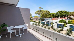 A balcony with a white table and chairs, a potted plant, and a view of a residential area with houses and greenery. - Bondi Beach Studios (Bondi)
