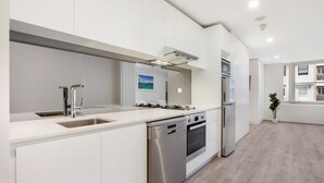 A modern kitchen with white cabinetry, stainless steel appliances, and a large window providing natural light. - Bondi Beach Studios (Bondi)