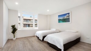 A modern hotel room with two beds, a large window with a view of buildings, and a potted plant. - Bondi Beach Studios (Bondi)