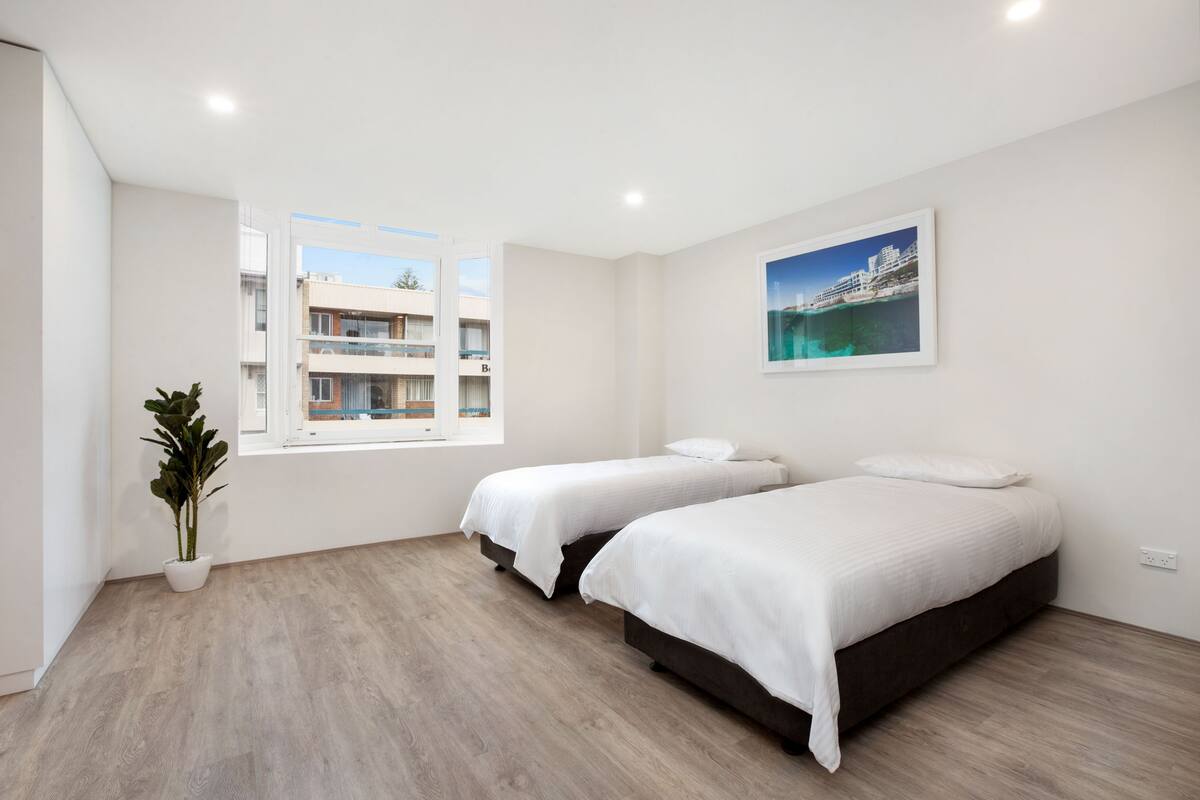Habitación de hotel moderna con dos camas, un ventanal con vistas a edificios y una planta en maceta.