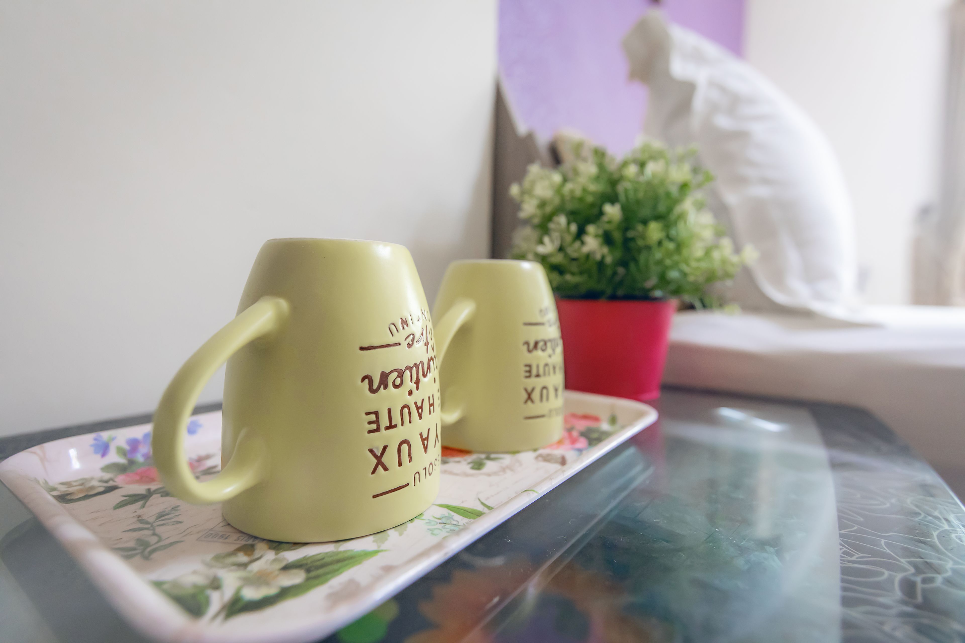 Two yellow mugs with text on a floral tray on a glass table.