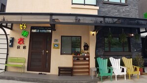 A two-story building with a beige facade, a balcony, and a storefront with a green bench and chairs outside. - Goodfriend B&B (Magong)