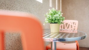 A round table with a potted plant, two orange chairs, and a concrete wall in the background. - Goodfriend B&B (Magong)