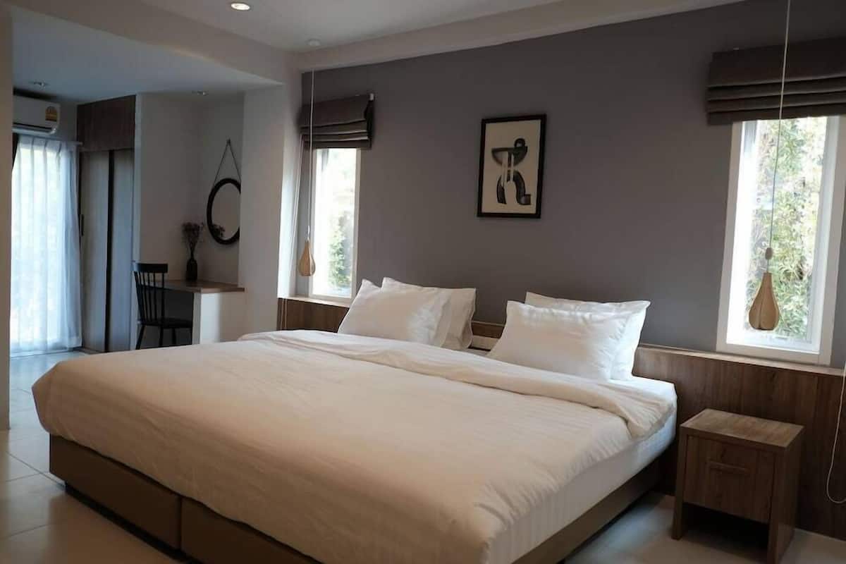 Un dormitorio con una cama grande, una mesita de noche, una silla y una ventana con cortinas.