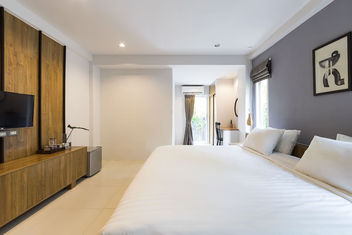 Habitación de hotel moderna con una cama grande, una mesa consola de madera, un televisor de pantalla plana y vistas al exterior.