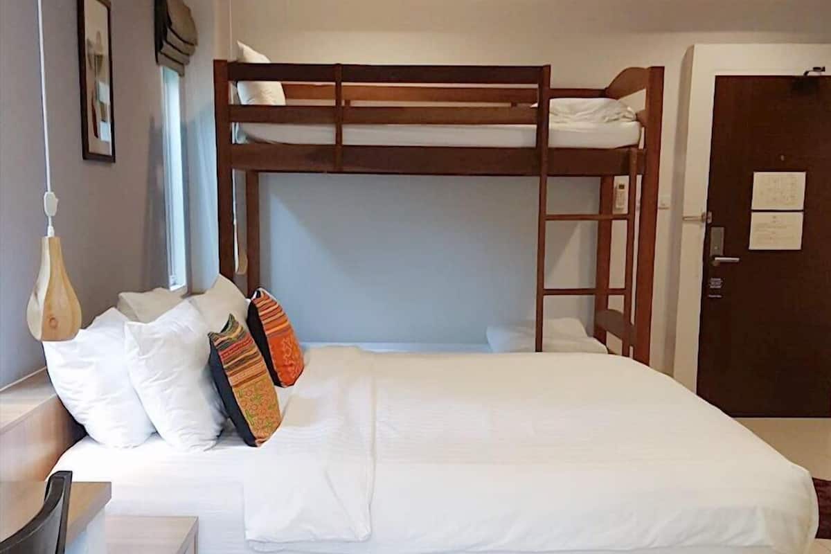 Una cama litera con ropa de cama blanca, un escritorio de madera, una silla y una pequeña cesta de mimbre en el suelo.