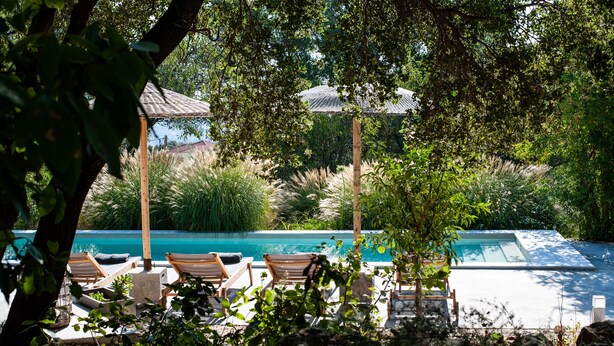 Un área de piscina con sillones de descanso y una pérgola, rodeada de exuberante vegetación.