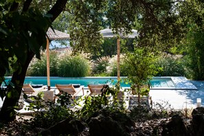 Área de piscina com espreguiçadeiras e um pergolado, cercada por vegetação exuberante.
