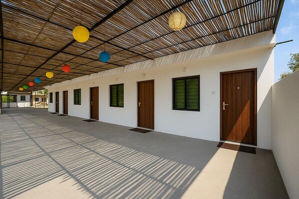 A covered walkway with multiple doors and windows, leading to individual rooms. - Stay Guru Resort Farm Villa (Bhuj)