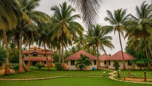 A resort with multiple bungalow-style buildings, surrounded by lush palm trees and well-maintained lawns. -  Stay Guru Resort Farm Villa (Bhuj)