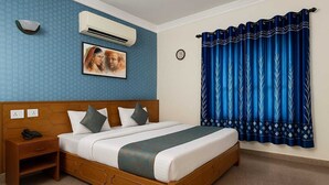 A hotel room with a wooden bed, a nightstand, an air conditioning unit, a clock, and blue curtains with a leaf pattern. -  Stay Guru Resort Farm Villa (Bhuj)
