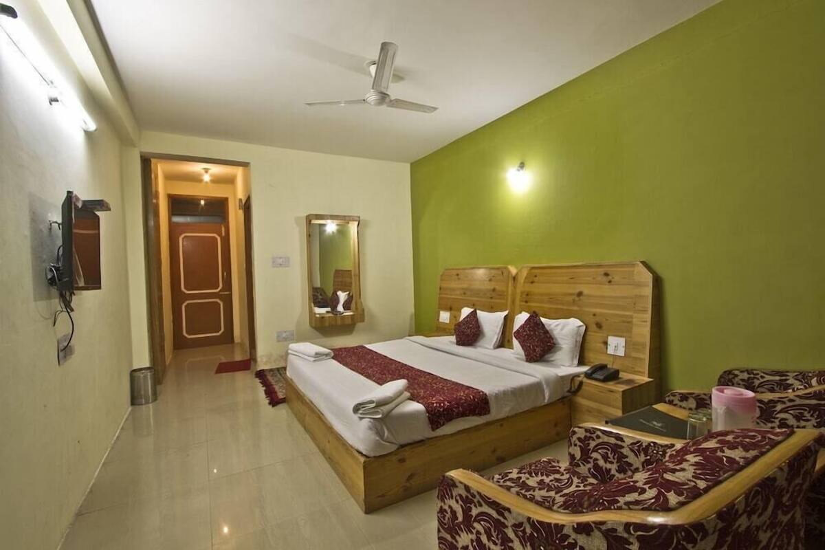 Un dormitorio con una cama de madera, una mesita de noche, una silla, un espejo y una puerta que da a otra habitación.