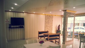 A dining area with a table and chairs, a television mounted on the wall, a Christmas tree, and a stone pillar. - Otel Turker (Sile)