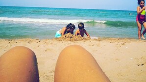 A beach scene with two children playing in the sand, a person standing in the water, and a clear blue sky. - Otel Turker (Sile)