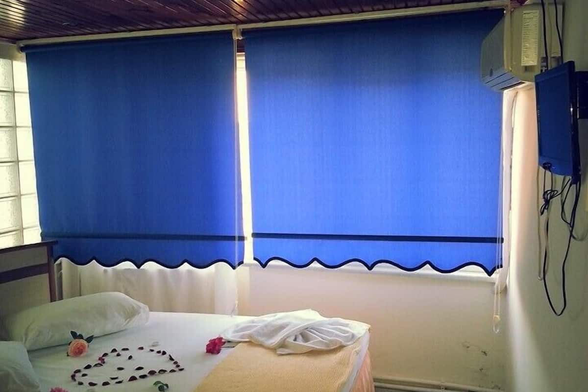 Une chambre avec un lit, une petite table sur laquelle se trouvent un verre et une télécommande, et un téléviseur fixé au mur.