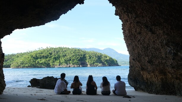 A group of people sitting on a beach with a view of a forested island and clear blue water. - Buena Lynne's Resort Annex (Puerto Galera)