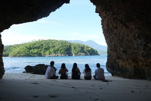A group of people sitting on a beach with a view of a forested island and clear blue water. - Buena Lynne's Resort Annex (Puerto Galera)