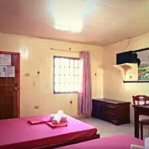 A room with a bed, a desk, a chair, a window with curtains, and a wall-mounted TV. - Buena Lynne's Resort Annex (Puerto Galera)