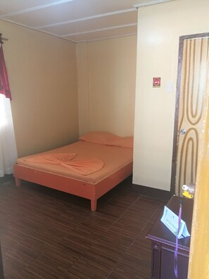 A small, single-bed room with a wooden floor, a plain wall, and a door with a 'No Smoking' sign. - Buena Lynne's Resort Annex (Puerto Galera)