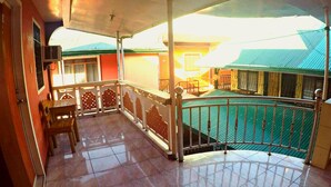A covered balcony with tiled flooring, a wooden table with chairs, and a railing. - Buena Lynne's Resort Annex (Puerto Galera)