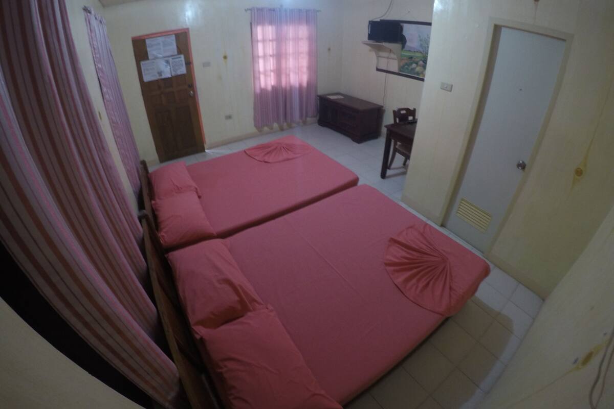 A room with two beds, a wooden cabinet, a small table, and a door.