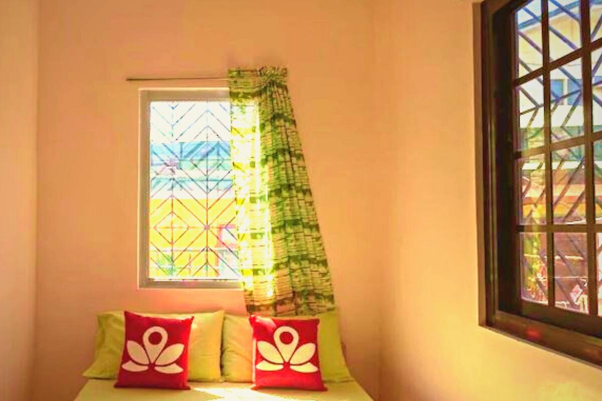 A room with a bed, a window with a curtain, and a view of buildings outside.