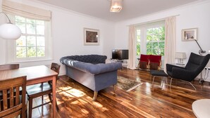 Una sala de estar con un sofá azul, una mesa de comedor de madera, sillas, un televisor y una butaca roja.