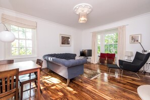 A modern living room with a sofa, a TV, and a dining area with a table and chairs. - Toast Stays - The Three Rosellas at The Grove (Durham)