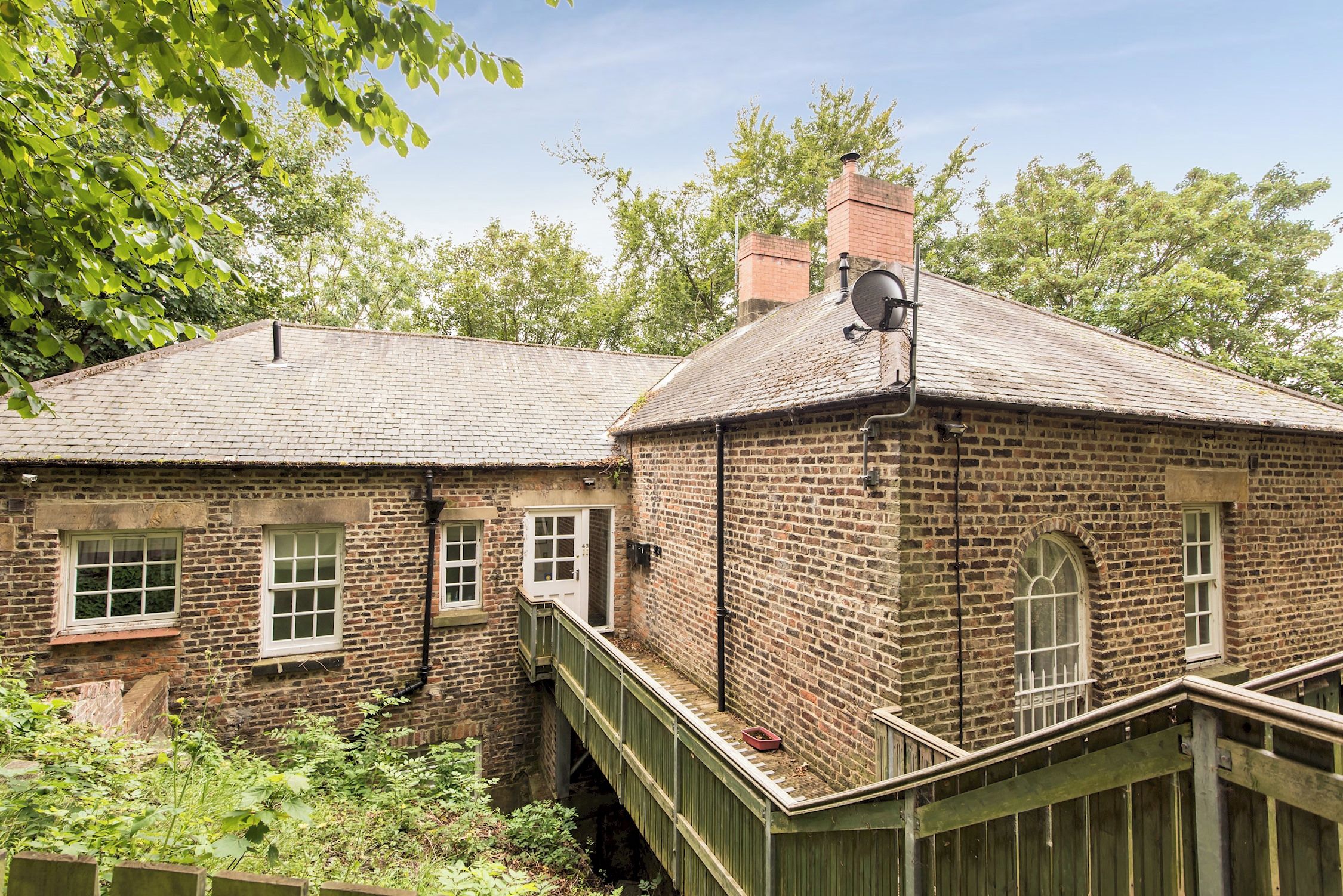 Un bâtiment en briques à l’architecture traditionnelle, doté d’une cheminée, d’une antenne parabolique et d’une petite fenêtre.