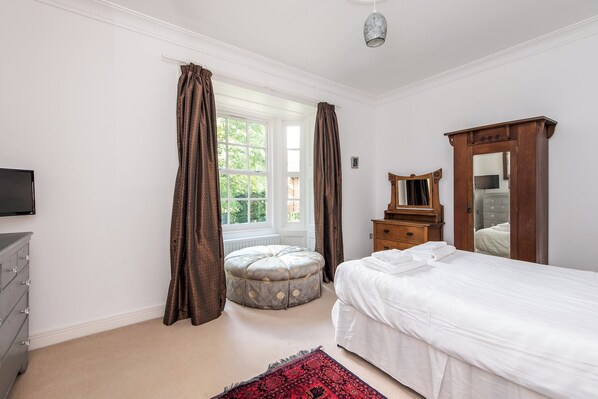 A bedroom with a bed, a dresser, a mirror, a window with curtains, and a television. - Toast Stays - The Three Rosellas at The Grove (Durham)