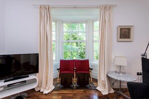 A room with a large window, two red chairs, a television, and a small table. - Toast Stays - The Three Rosellas at The Grove (Durham)