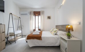 A bedroom with a bed, a nightstand, a lamp, a ladder, and a window with curtains.