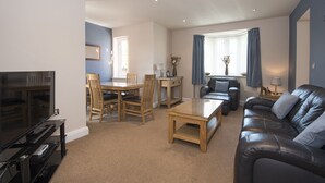 A modern living room with a flat-screen TV, wooden furniture, a leather sofa, and a dining area with a table and chairs. - Toast Lettings | Milbungate View - Durham City (Durham)