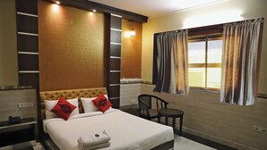 A hotel room with a large bed, a chair, a small table, and a window with curtains.