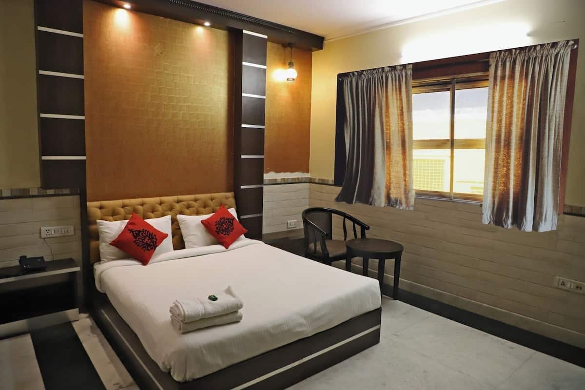 A hotel room with a large bed, a chair, a small table, and a window with curtains.