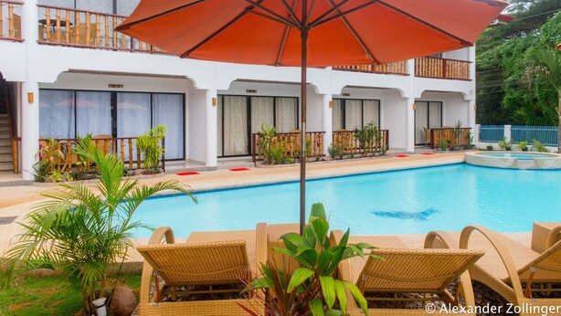 A poolside area with lounge chairs and an umbrella, surrounded by a building with balconies and windows. - Alona Vida Beach Hill (Panglao)