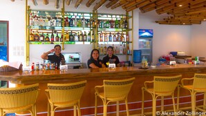 A bar area with wicker chairs, a shelf of various liquor bottles, and a bamboo ceiling. - Alona Vida Beach Hill (Panglao)