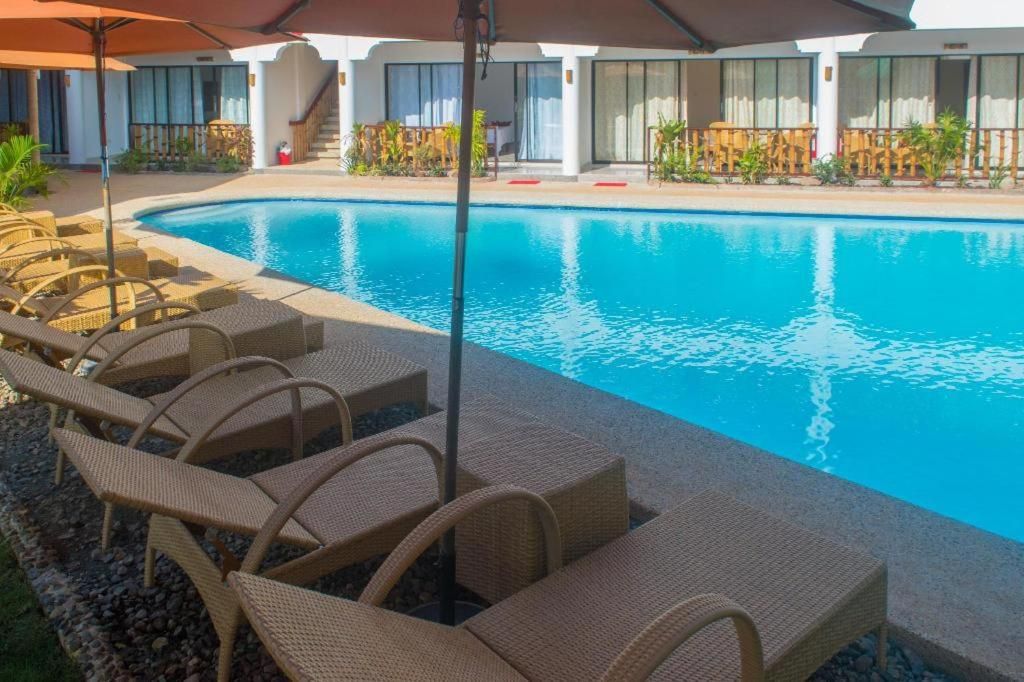 A swimming pool with lounge chairs and umbrellas, surrounded by a building with large windows and a covered walkway.