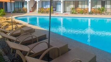A swimming pool with lounge chairs and umbrellas, surrounded by a building with large windows and a covered walkway.