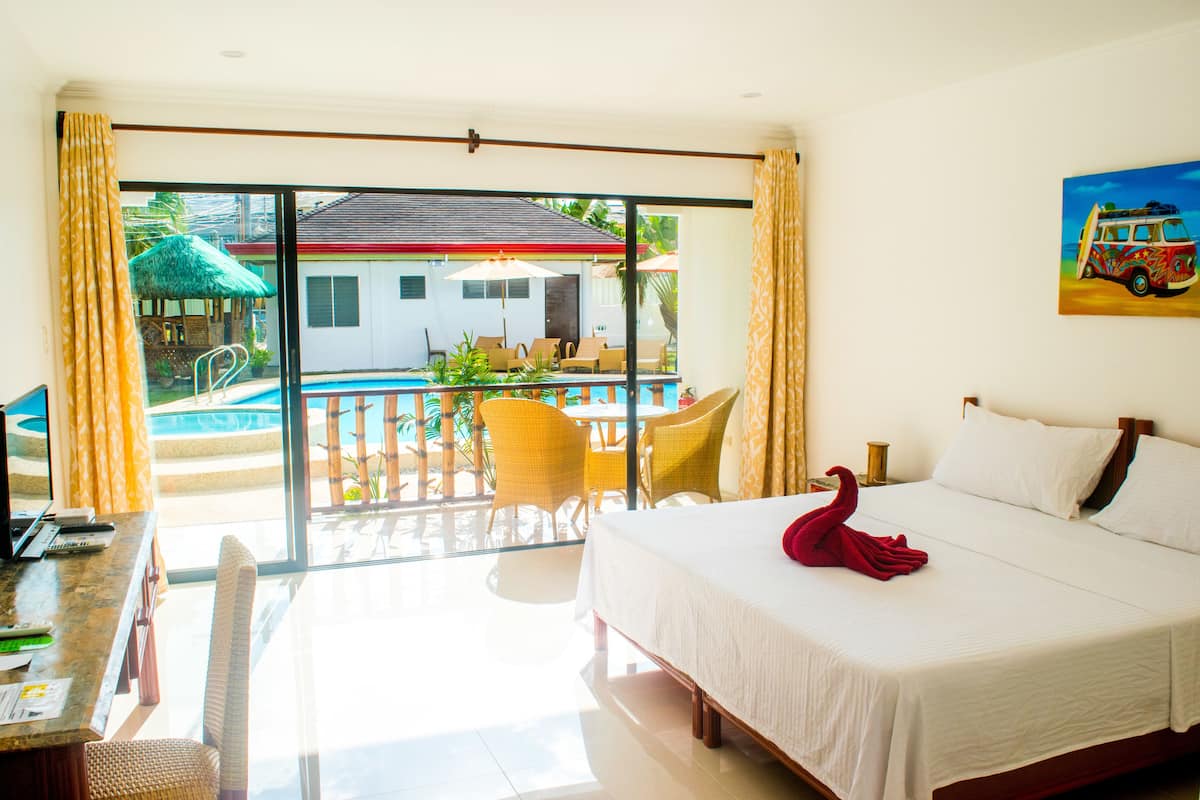 A hotel room with a bed, a desk with a laptop, a dining area with chairs and a table, and a view of a pool and building outside.