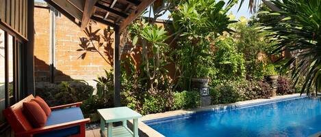 A poolside area with a wooden deck, a red and blue lounge chair, and a small table.