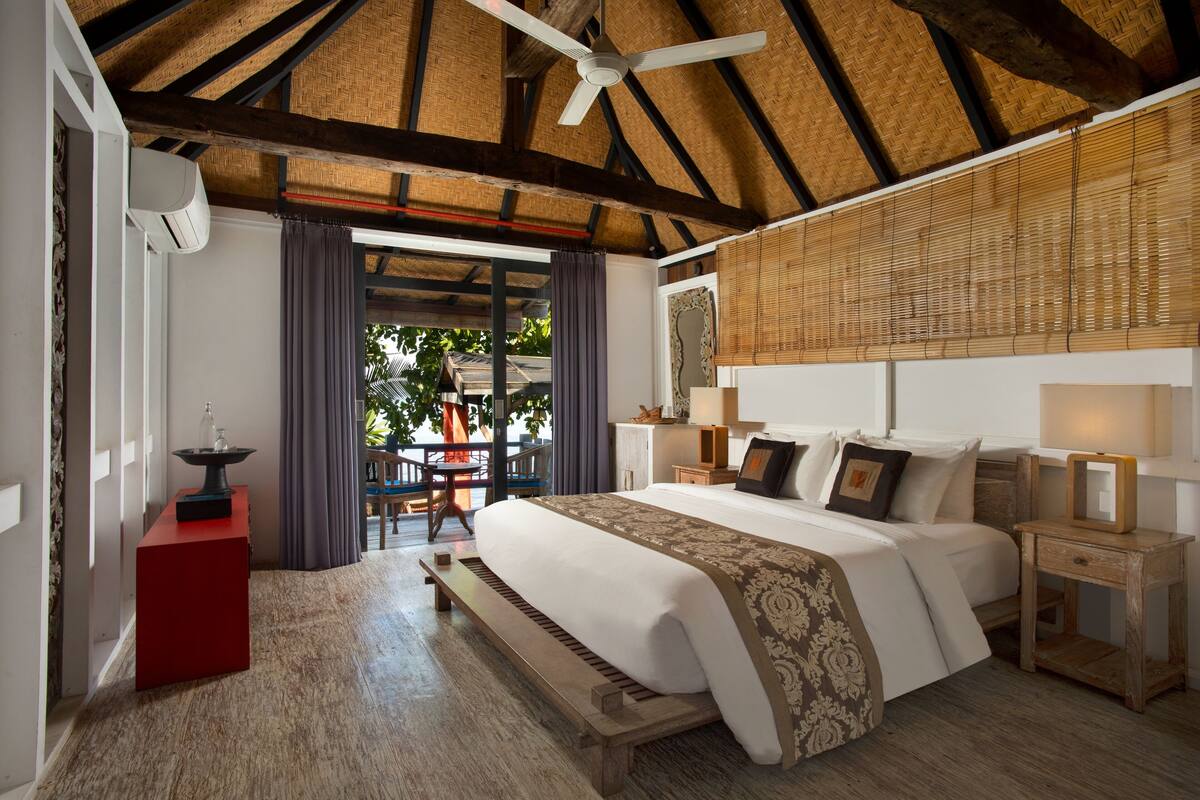 A bedroom with a large bed, a ceiling fan, a red cabinet, and a view of the outdoors.