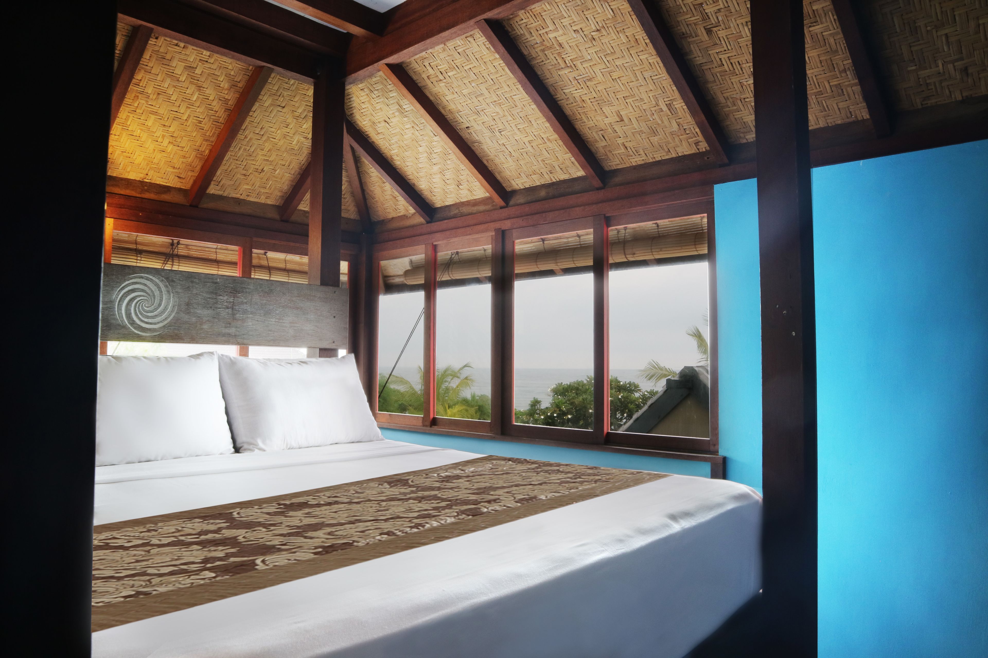 A bedroom with a large bed, a wooden ceiling, and a view of the ocean.
