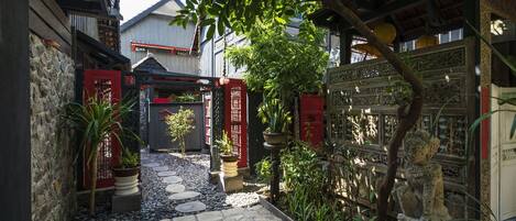 A narrow stone pathway leading to a traditional building with red gates and potted plants.