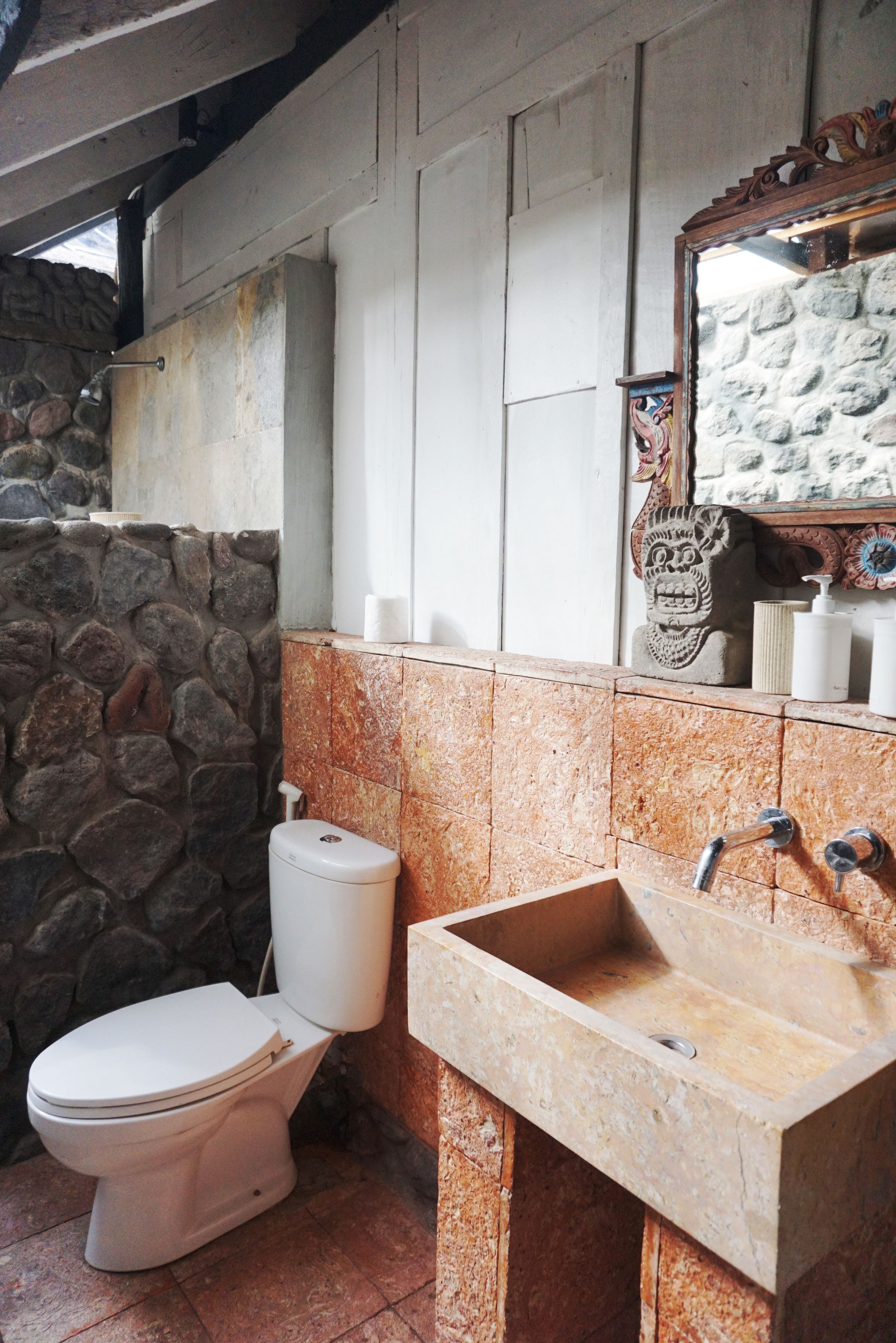 A bathroom with a stone wall, a toilet, a sink, and a mirror.