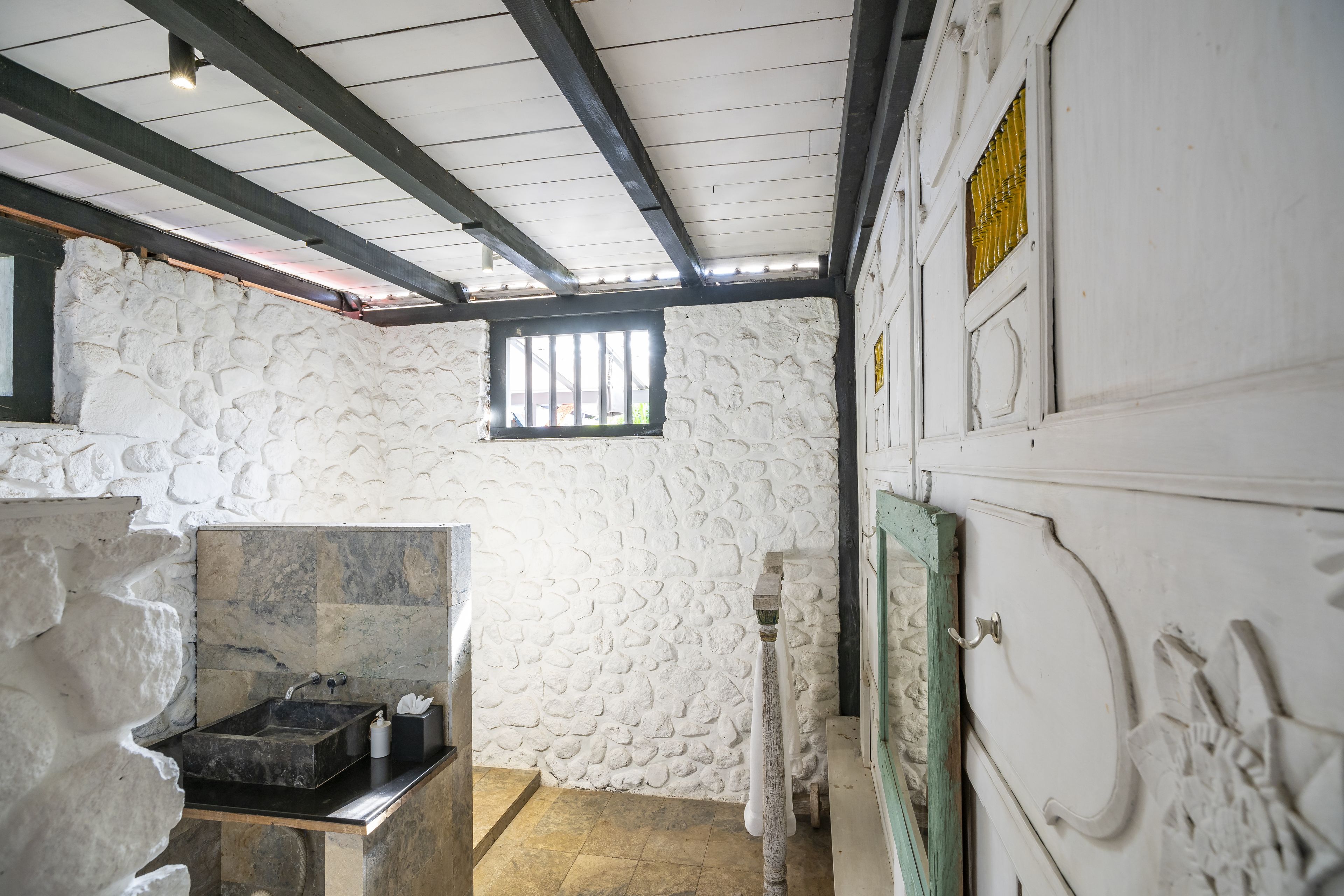 A stone-walled room with a sink, a window, and a door with intricate carvings.