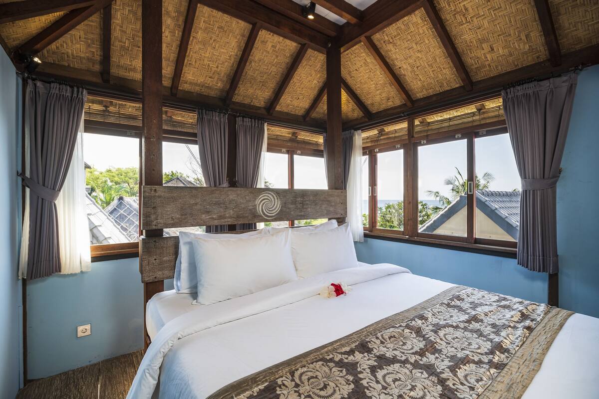 A bedroom with a bed, wooden headboard, and large windows with curtains.
