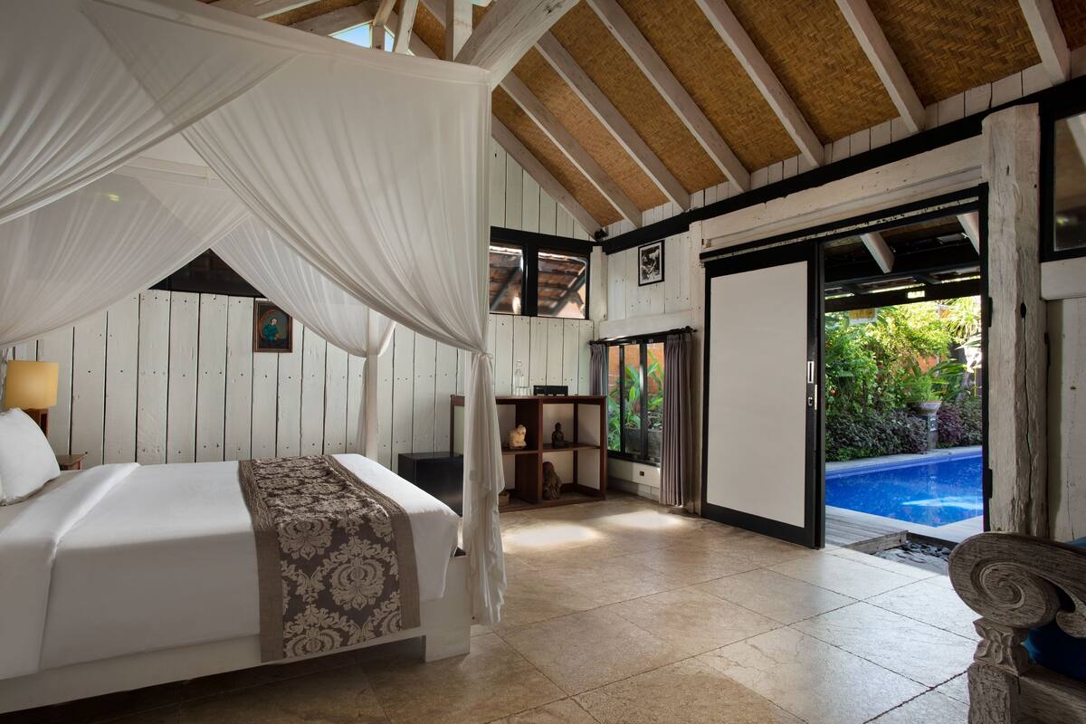 A bedroom with a canopy bed, a wooden desk, and a view of an outdoor swimming pool.